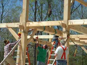 Setting a girt.
This photo shows a girt being flown in and being set on two splines and two braces. This girt is one of the ones that will support the hallway floor joists. You can see the floor joist pockets in the side of the girt near the straps.
